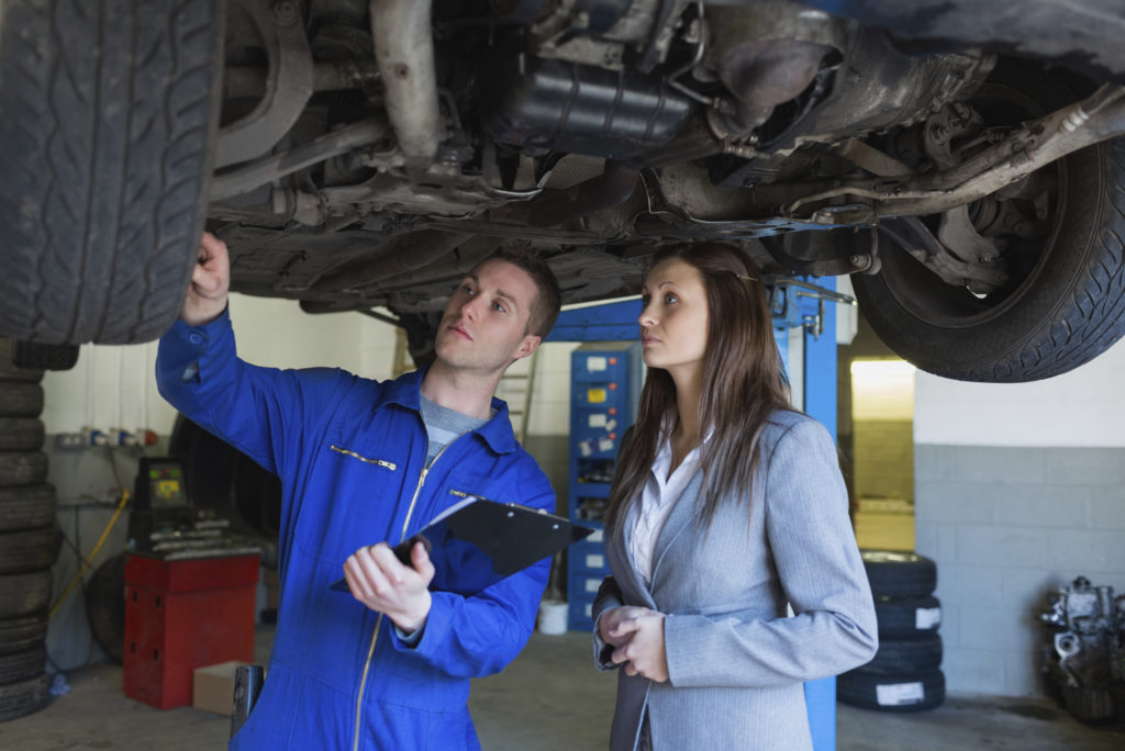 Auto mechanic and woman examining car tire in garage